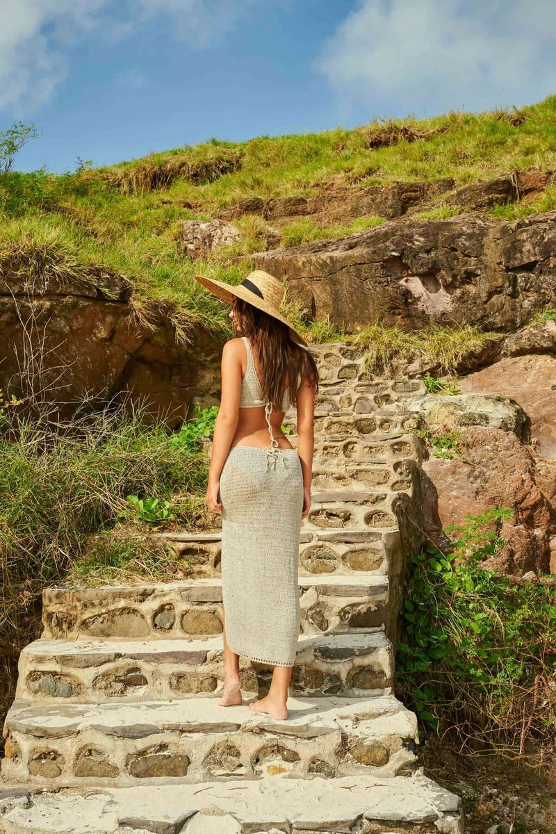 a model on stone steps in a beige crochet skirt and top and a wide-brimmed hat