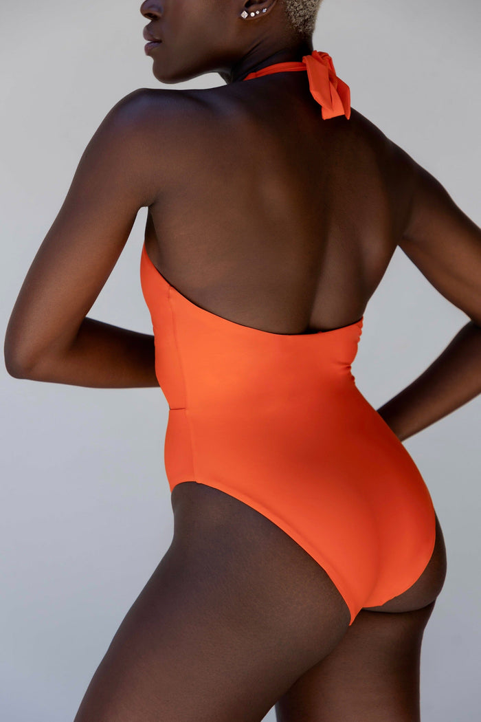 a model showing the back of an orange monokini swimsuit